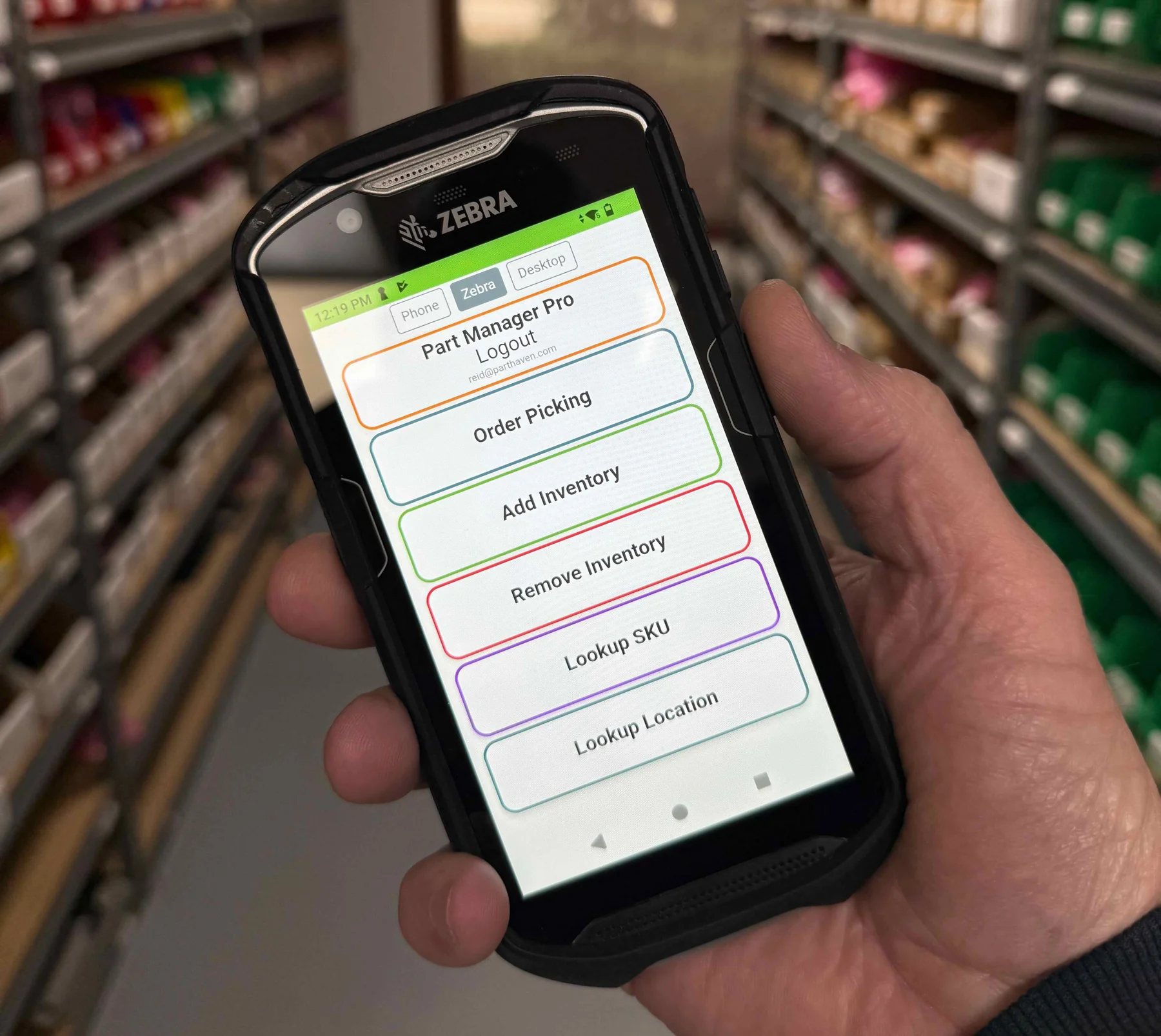 A Zebra TC-series handheld showing the Part Manager Pro home screen, held in a parts warehouse aisle